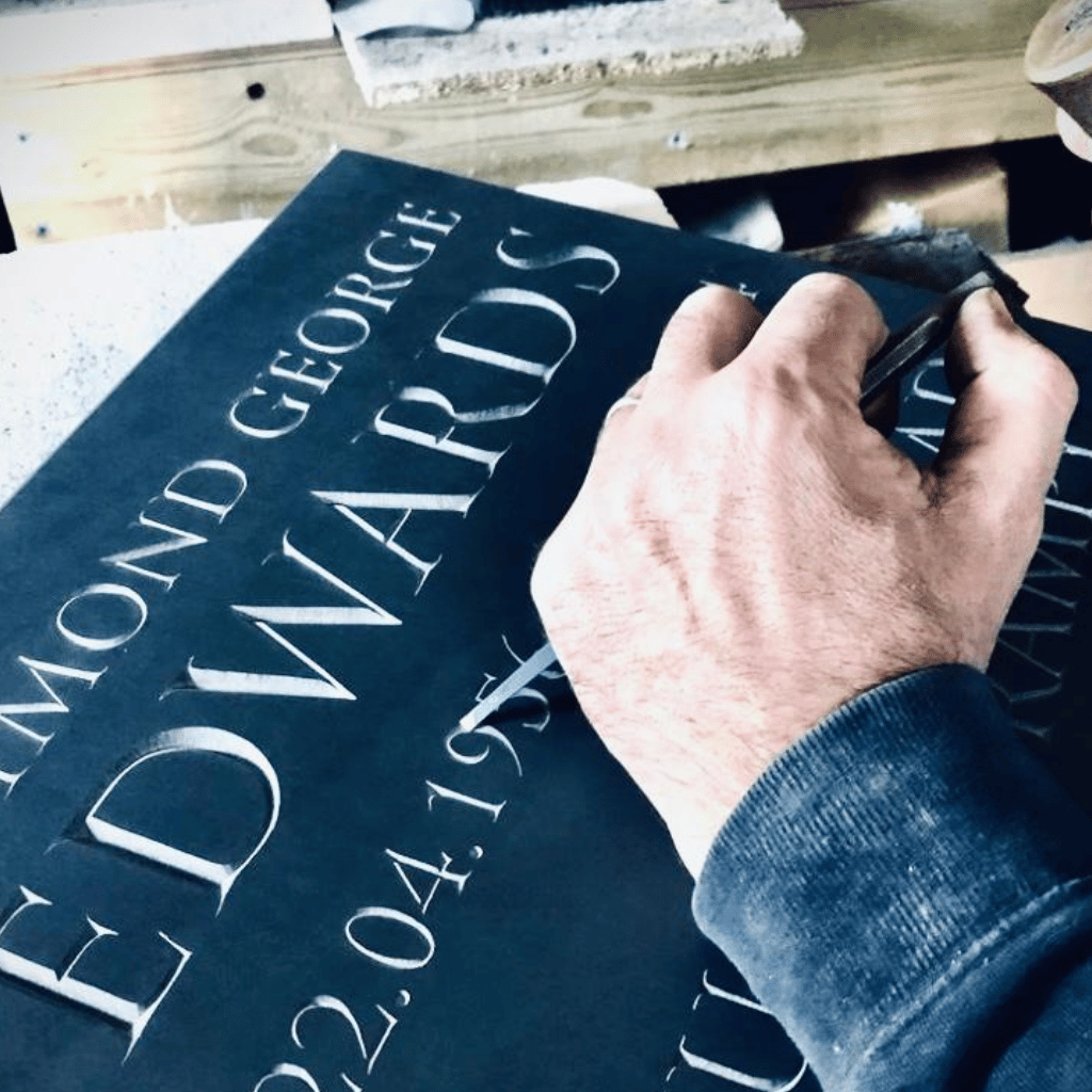 A memorial mason hand-finishing lettering on a dark stone memorial