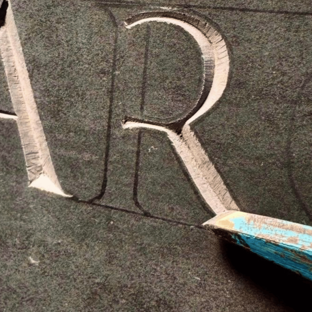 Close-up of a hand-cut letter being carved into dark memorial stone